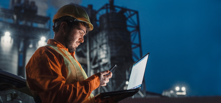 Factory worker holding laptop in front of oil refinery